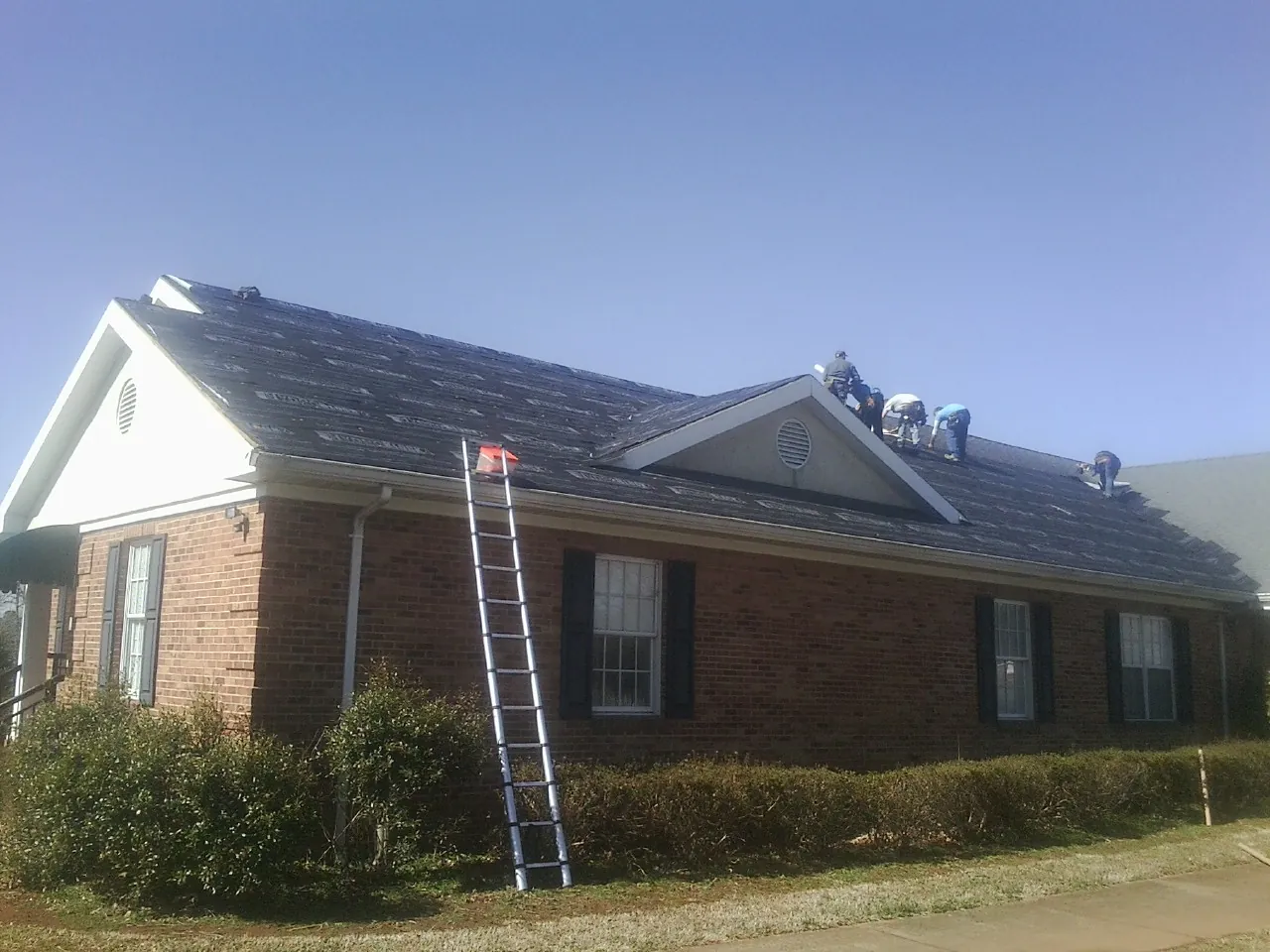 Crew tearing shingles off a brick ranch roof with a ladder set — Emergency Roof Repair work by our crew in Chokoloskee