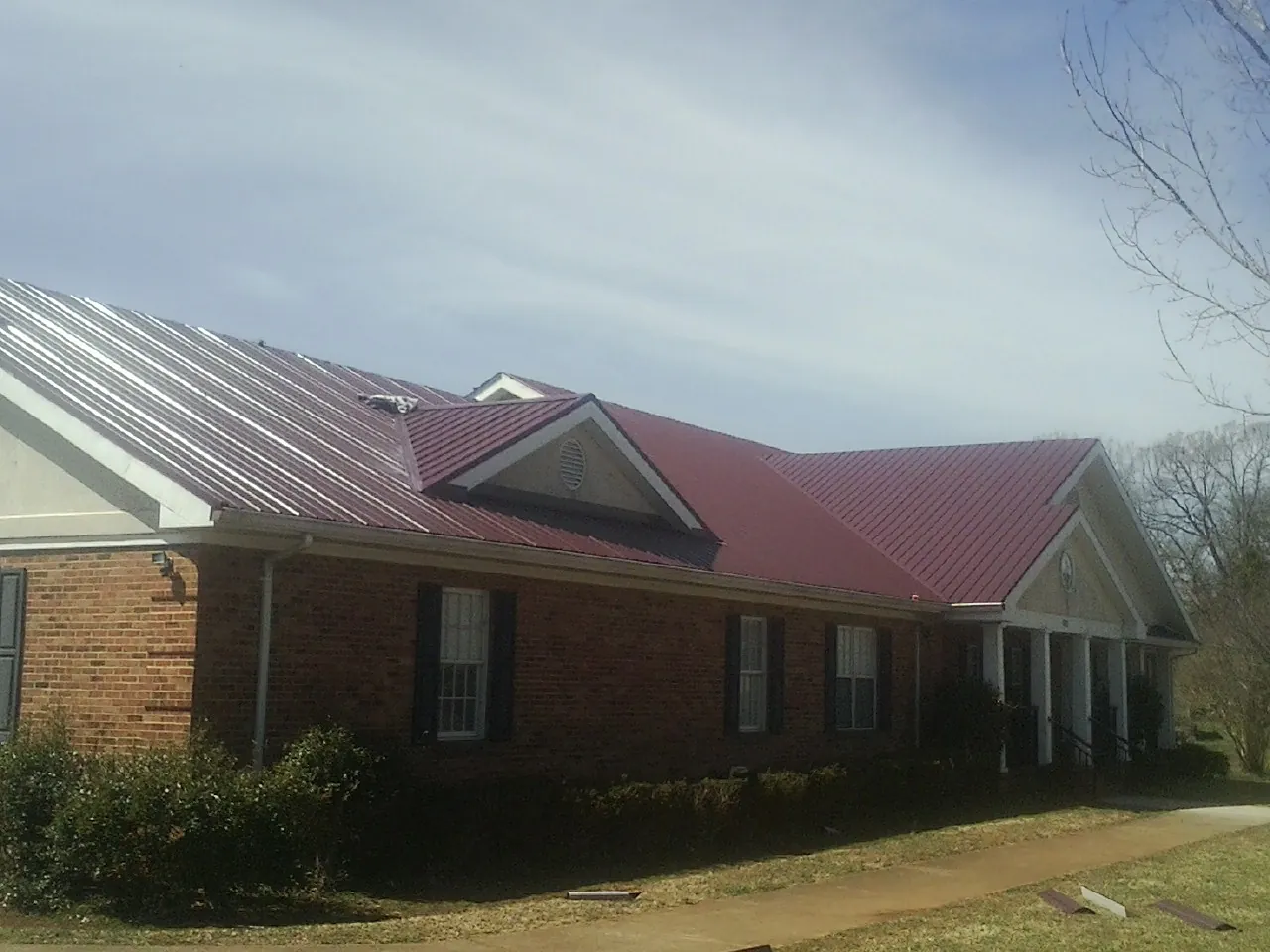 Red metal roof with gabled entries on a long brick building, from a Hail Damage Roof Repair job in Chokoloskee