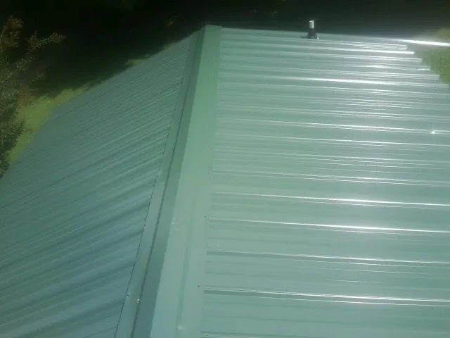 New green metal panels meeting at the ridge of a roof — Flat Roof Repair work by our crew in Chokoloskee