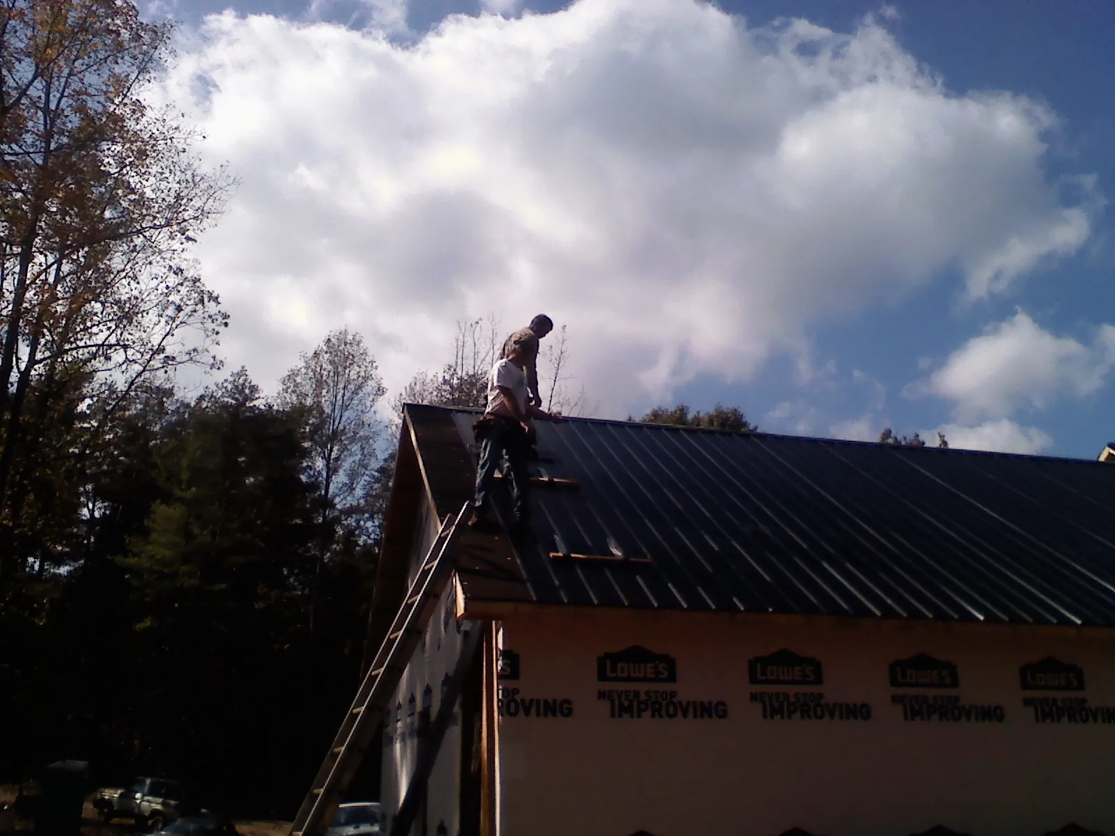 Roofer fastening dark metal panels high against a cloudy sky, from a Roof Inspection job in Chokoloskee